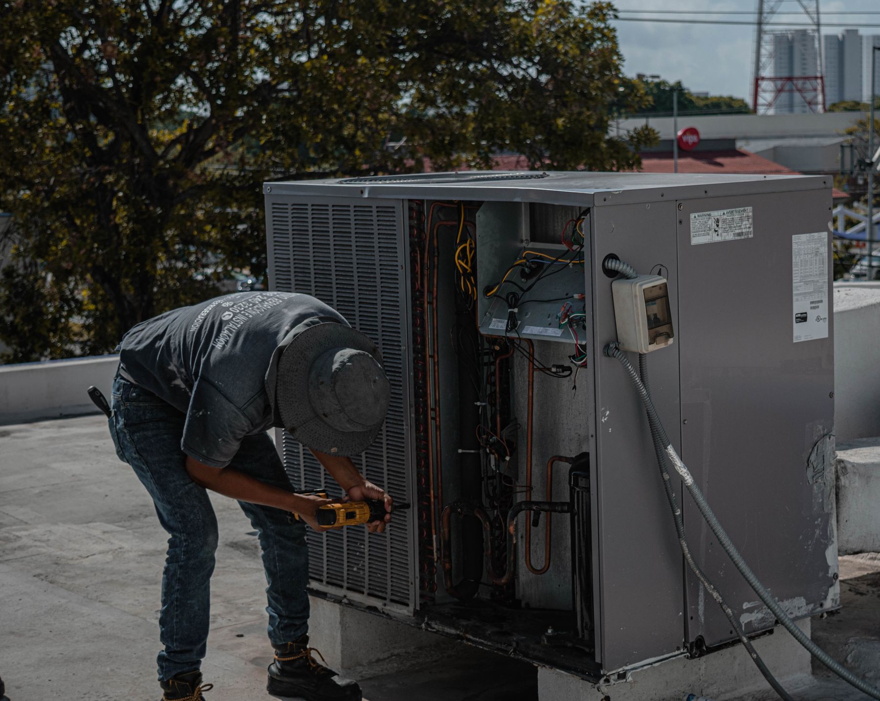 HVAC technician servicing an open packaged rooftop unit on a commercial building
